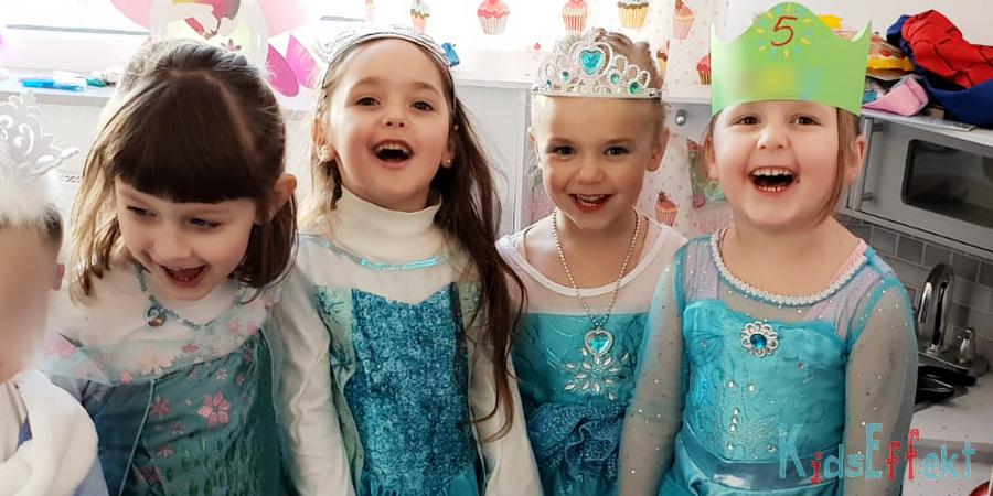 Kleine Mädchen strahlen in die Kamera. Sie tragen Eisköniginkostüme und freuen sich über den Besuch der echten Eisprinzessin zum Geburtstag